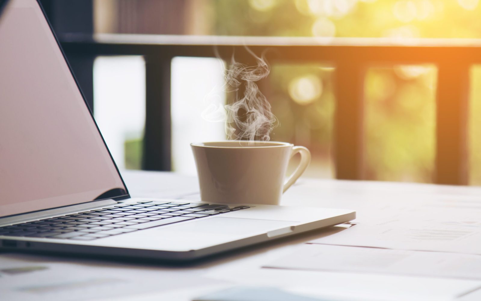 gőzölgő kávé egy laptop mellett egy teraszon